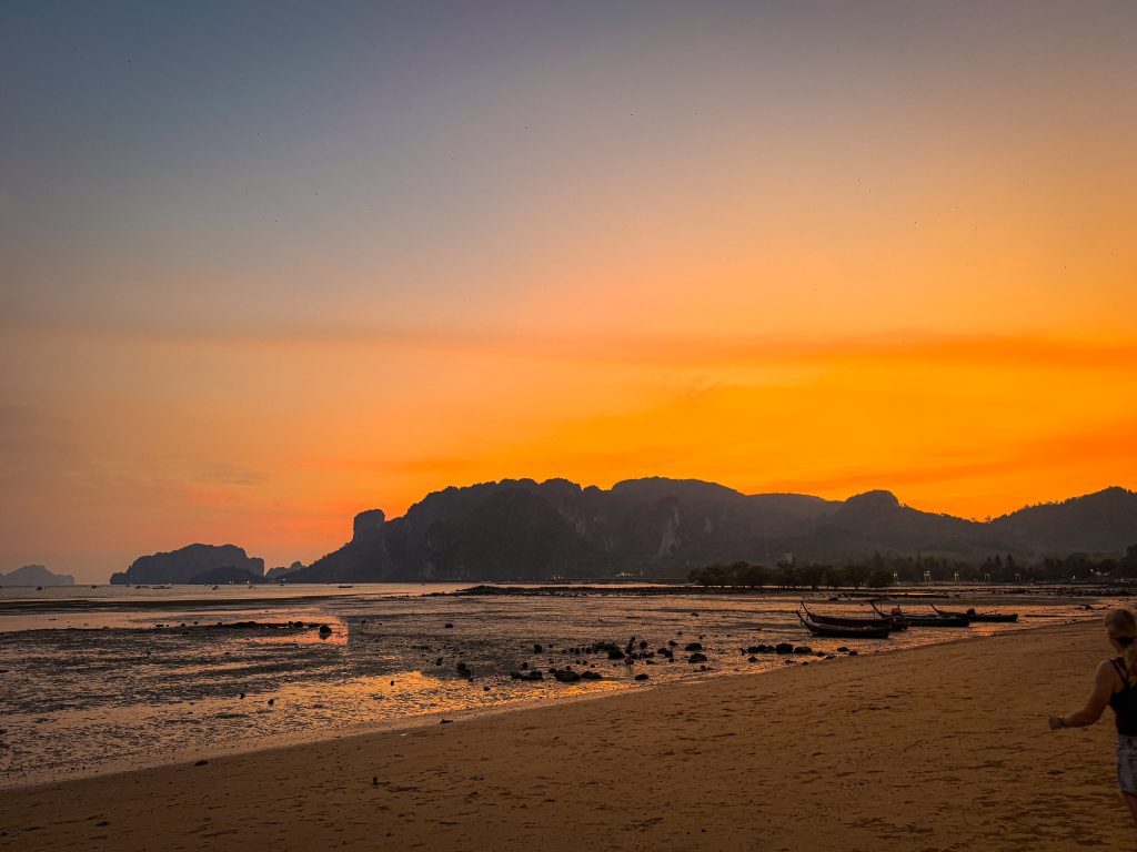 Orange sunset over limestone cliffs and longtail boats viewed from Joy Thai Food in Krabi.