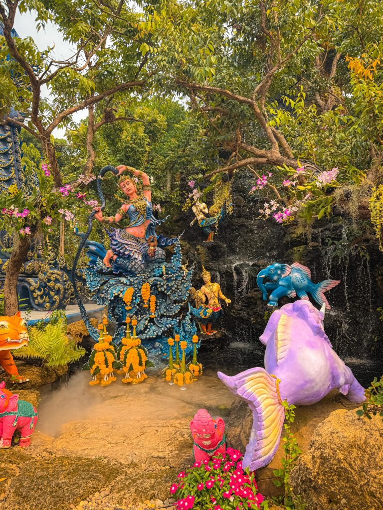 Colorful garden sculptures, flowers, and a waterfall display at the Blue Temple complex in Chiang Rai.