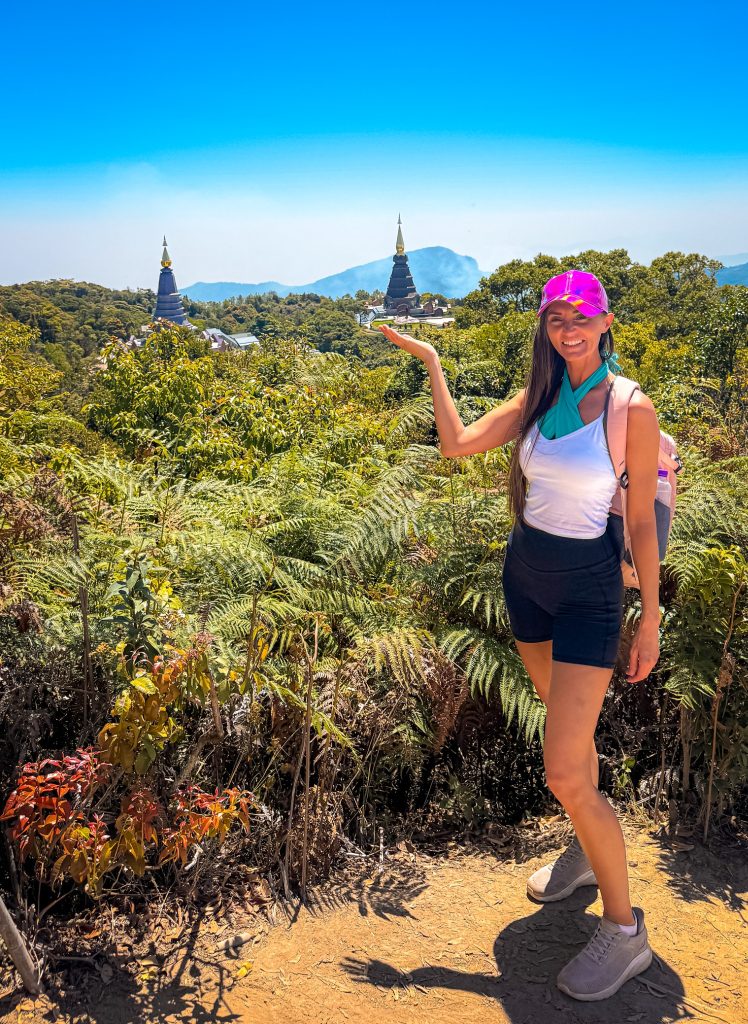 Traveler posing at a viewpoint with the Royal Twin Pagodas visible across the forest in Doi Inthanon National Park.