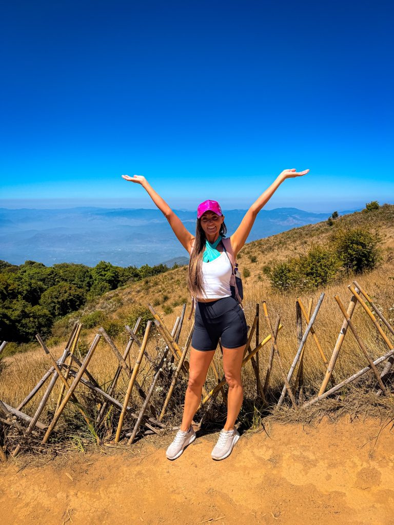 Traveler with arms up on a mountain trail surrounded by sweeping views during a Doi Inthanon trekking experience near Chiang Mai.