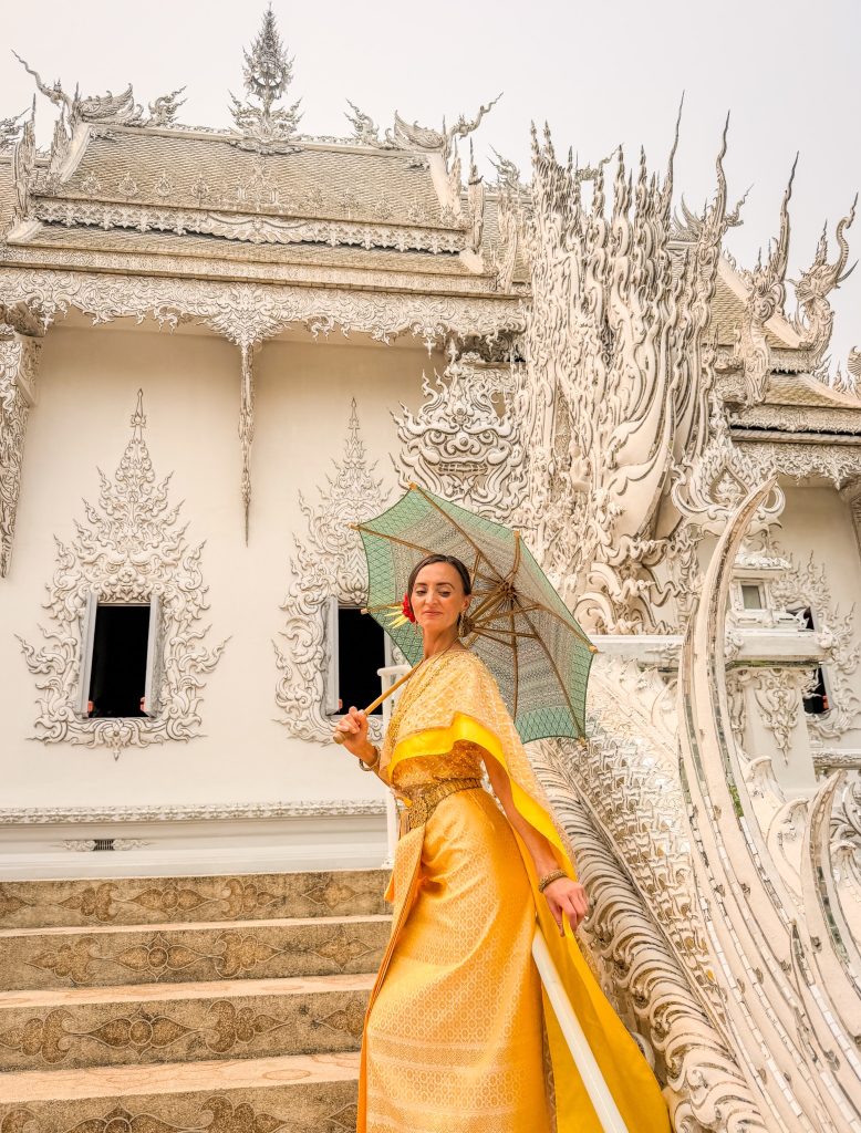Woman in a gold traditional Thai dress holding a green parasol on the ornate stairs at the White Temple.