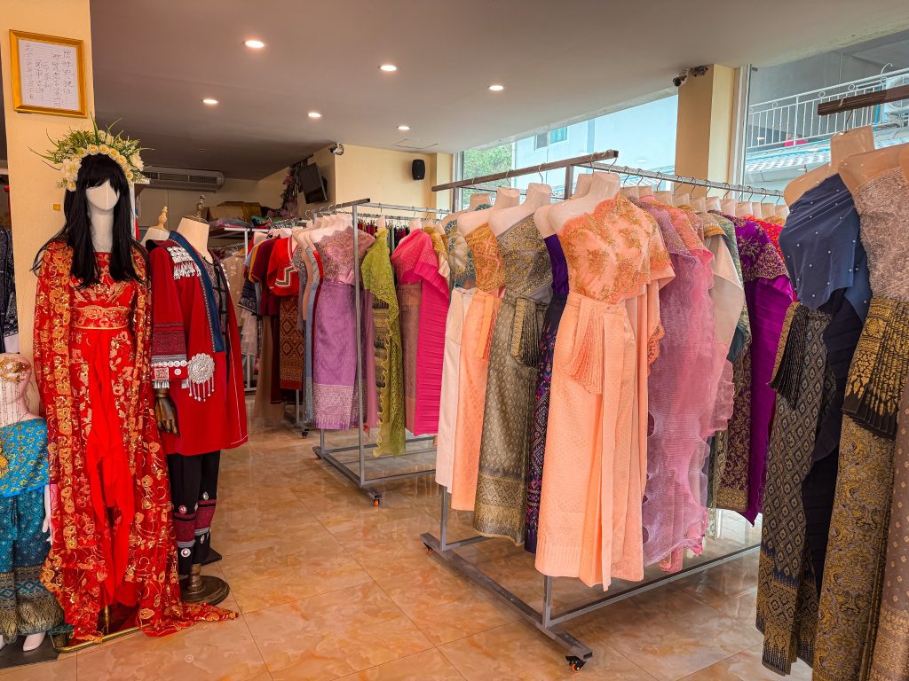 Racks of colorful traditional Thai dresses and embroidered outfits inside a Chiang Rai rental shop.