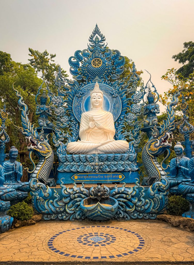 White seated Buddha surrounded by elaborate blue sculptures and guardian figures in Chiang Rai.
