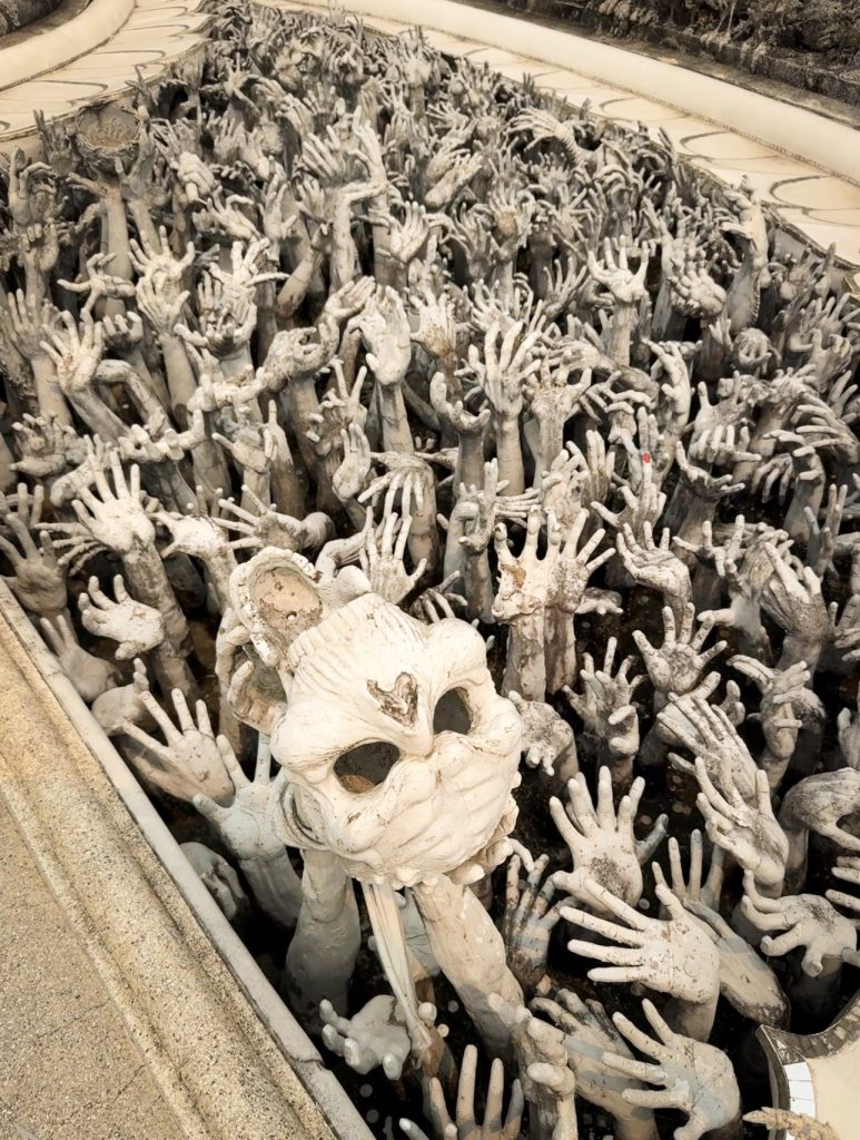 Skull and reaching hand sculptures surrounding the bridge at the White Temple in Chiang Rai.