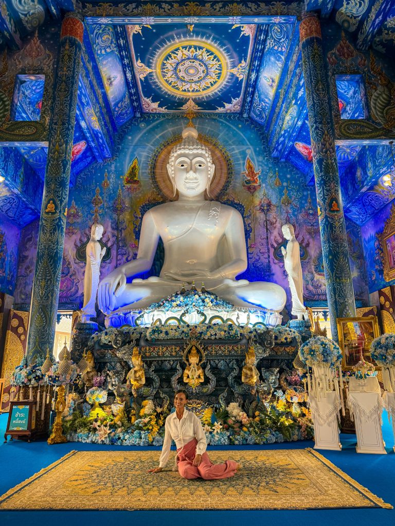 Woman in a white shirt and pink pants sitting beneath the large white Buddha inside the Blue Temple in Chiang Rai.